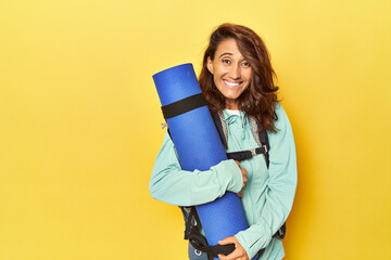 Middle aged woman with mountain backpack and mat on yellow