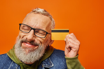 Wall Mural - handsome mature male model in vibrant clothing posing with closed eyes and holding credit card