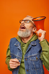 Wall Mural - shocked fashionable mature man in vibrant outfit with glasses posing with megaphone near his head