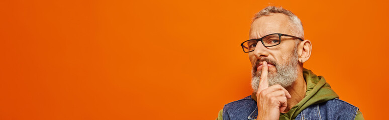 Wall Mural - focused mature man in green hoodie with glasses and gray beard posing on orange background, banner