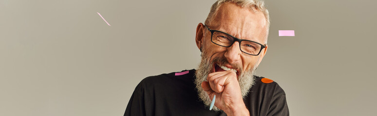 Wall Mural - jolly mature man in black t shirt with glasses biting his fist posing under confetti rain, banner