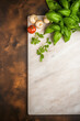 Mockup of a vacant wooden cutting board with a bordered design frame, surrounded by fresh ingredients. Vegan composition exhibited against a dark contemporary kitchen surface.