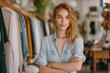 © tonstock - Blond fashion business owner poses confidently in her boutique, surrounded by apparel on hangers, ready to help clients choose their perfect outfit.