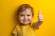 © tonstock - A toddler in a diaper gives a cheerful thumbs up on a vibrant yellow background, showing approval and encouragement with a happy smile.