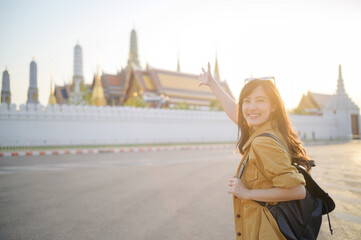 Wall Mural - Traveler asian woman in her 30s, backpack slung over her shoulder, explores the intricate details of Wat Pra Kaew with childlike wonder. Sunlight dances on the golden rooftops.