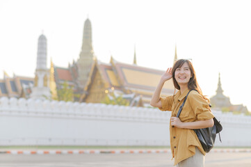 Wall Mural - Traveler asian woman in her 30s, backpack slung over her shoulder, explores the intricate details of Wat Pra Kaew with childlike wonder. Sunlight dances on the golden rooftops.