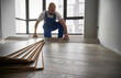 © anatoliy_gleb - Selective focus of laminate wooden planks and male construction worker on blurred background. Mane installing laminate timber floor in apartment under renovation.