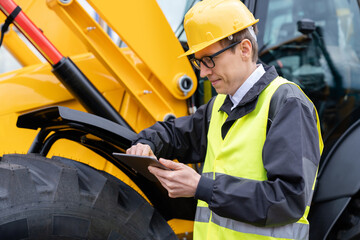Aufkleber - Engineer in a helmet with a digital tablet stands next to construction excavators..