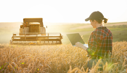 Poster - Female farmer with laptop on a background of harvester. Smart farming concept