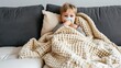 © Stavros - Little sick girl sits on the couch at home and blows her nose. On the couch, a sick girl finds solace in the gentle embrace of her favorite blanket.