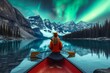 A lone figure navigates the tranquil lake, her paddle slicing through the crystal waters as she takes in the majestic winter landscape of snow-capped mountains and dancing northern lights from her tr