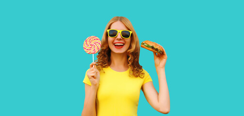 Wall Mural - Portrait of happy cheerful young woman with burger fast food and sweet lollipop