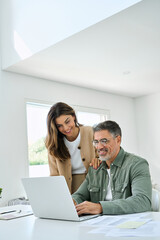 happy mature older couple using laptop technology at home. smiling middle aged senior man working on