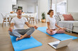 © insta_photos - Happy calm senior couple, serene healthy middle aged older man and woman doing yoga training exercises meditating learning yoga online class together using laptop computer at home in living room.