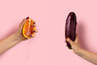 Female hand with half of juicy orange and eggplant on pink background. Sex concept.