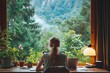 © dee-nesia - back view of a woman freelancer working on her laptop. In front of her is a large window with a green and calming forest view in a mountain.