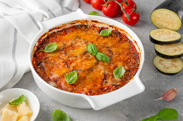 Wall Mural - Eggplant casserole with cheese and tomato sauce in a white baking dish on a gray concrete background with ingredients for cooking. Vegetarian healthy food.