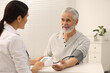 © New Africa - Nurse measuring elderly patient's blood pressure at white table in hospital