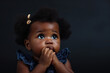 Scared African American baby girl and biting nails in studio with oops reaction on black background.