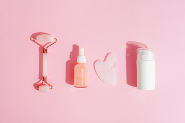 Wall Mural - Cosmetic cream and serum bottles, facial roller and gua sha stone on pink background with shadows. Skin care concept. Top view, flat lay