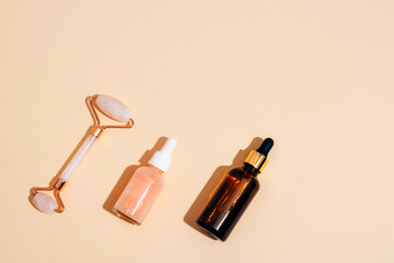 Wall Mural - Cosmetic serum bottles and facial roller on beige background with sharp shadows. Skin care concept. Top view, flat lay, copy space