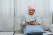 © Ekkasit A Siam - young woman assists  mother, a cancer patient, with technology, offering comfort on the sofa at home. daughter helps her ill mother use smartphone, providing solace and connection in their living room