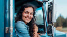 A Smiling Truck Driver Woman In A Denim Jacket Leaning Out Of A Truck's Window
