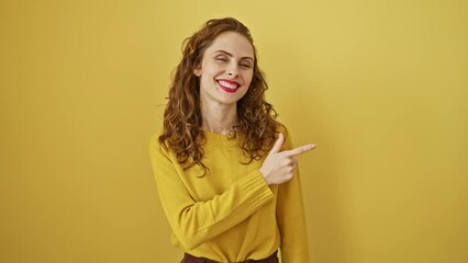 Wall Mural - Cheerful, young woman points up with a smiling face, presenting something off-side on a bright, yellow, isolated background