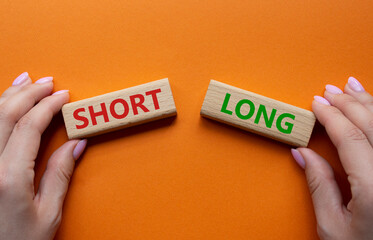 Short vs Long symbol. Concept word Short vs Long on wooden blocks. Businessman hand. Beautiful orange background. Business and Short vs Long concept. Copy space