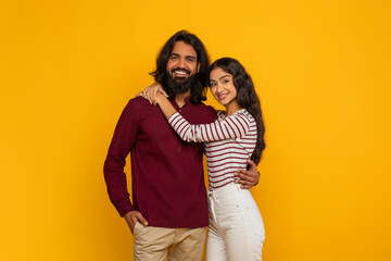 Wall Mural - Happy young indian man and woman embracing on yellow background