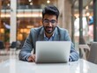 © buraratn - indian businessman working on laptop in modern office lobby space. Young indian student using computer remote studying, watching online webinar, zoom virtual training on video call meeting.