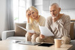 © Prostock-studio - Senior Couple Checking Financial Documents, Sitting On Couch At Home