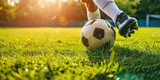 Fototapeta Sport - Football Player in Action on a Sunny Day. Close-up of a classic soccer ball on a lush green field with a player's foot in motion, sunlight background, copy space.