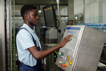 Poster - young african american worker standing in front of display of factory equipment or automated product