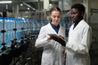 © pressmaster - Young engineers of bottled water factory in labcoats looking at tablet screen while discussing information or sketch of machinery