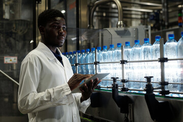 Poster - quality control inspector with tablet standing in front of conveyor belt with capped bottles of mine