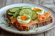 Danish cuisine Smorrebrod open sandwich with salmon cream cheese quail egg cucumber on white plate with wood backdrop