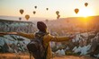 © Mr. Bolota - Happy Tourist Woman Experiencing the magical sunrise in Cappadocia with colorful hot air balloons in the sky, Turkey.