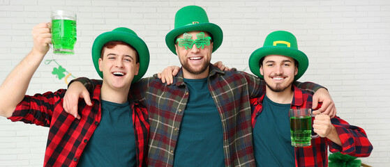 Canvas Print - Happy young men with mugs of green beer on light background. St. Patrick's Day celebration