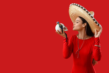 Poster - Beautiful woman in sombrero hat and with painted skull on red background. Mexico's Day of the Dead (El Dia de Muertos)