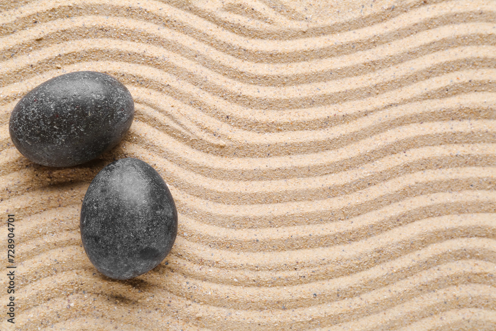 Black spa stones on sand with lines, closeup. Zen concept
