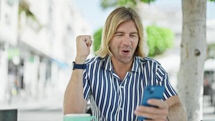 Sticker - Blond man in striped shirt feeling happy while using smartphone at outdoor café terrace.