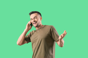 happy young man talking by mobile phone on green background