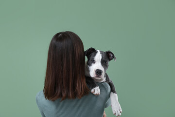 Beautiful young woman with cute staffordshire terrier puppy on green background, back view