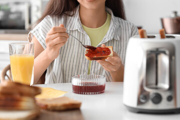 Poster - Young beautiful woman drinking orange juice and eating tasty toast with jam in kitchen, closeup