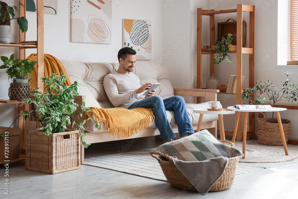 Handsome man with tablet computer resting on white sofa in modern living room