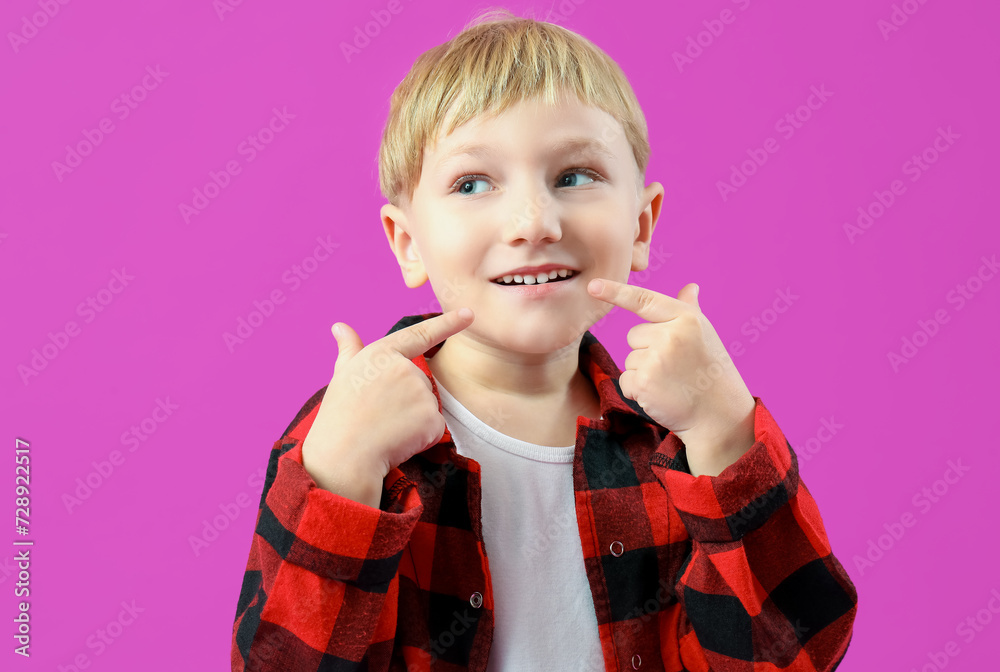 Happy little boy pointing at healthy teeth on purple background
