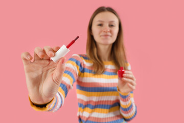 Wall Mural - young woman with bottle of red nail polish on pink background