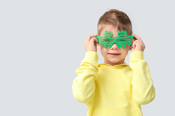 Cute little boy in decorative glasses in shape of clover on grey background. St. Patrick's Day celebration