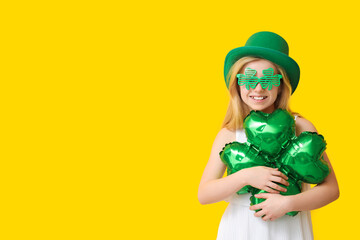 Wall Mural - Cute little girl in leprechaun hat and decorative glasses with air balloon in shape of clover on yellow background. St. Patrick's Day celebration